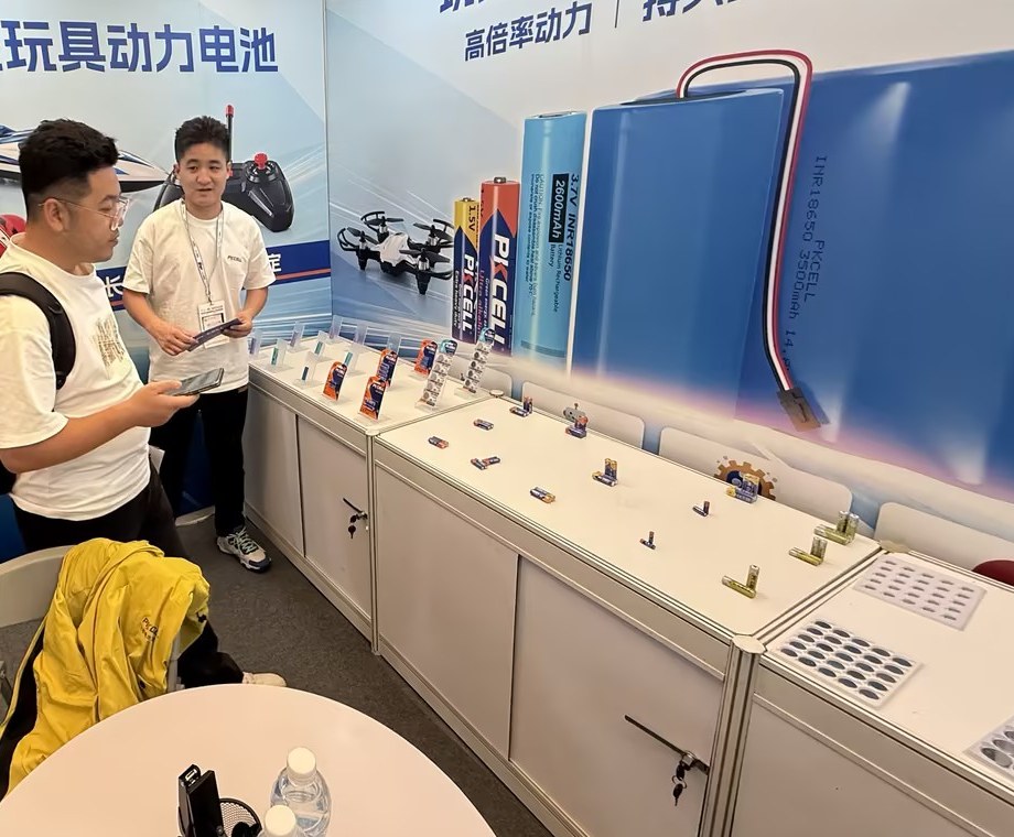 PKCELL玩具展展台陈列电池样品，工作人员与来访者围绕产品进行交流。